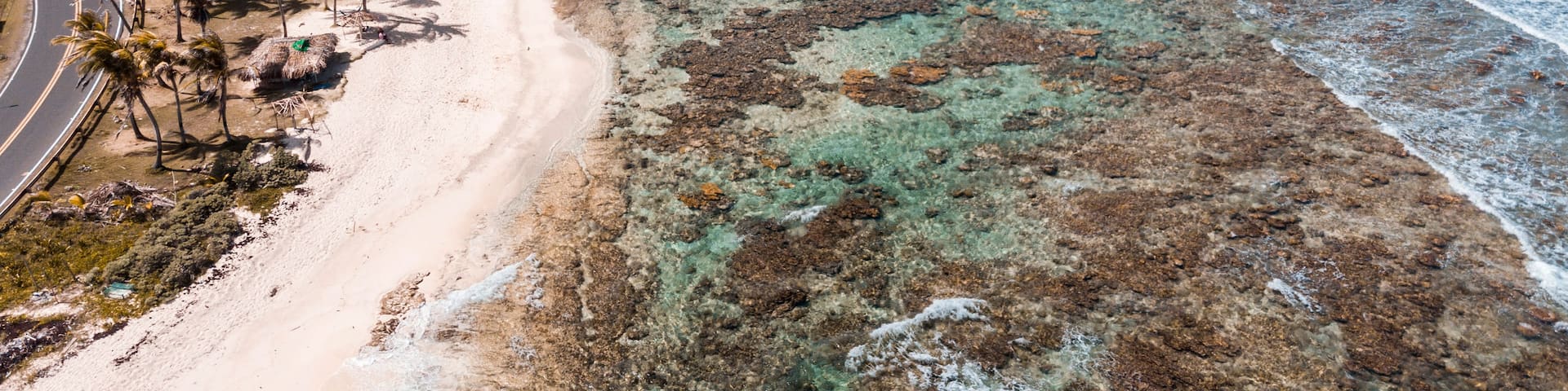 A coastal landscape with a sandy beach, clear turquoise waters, and rocky areas.