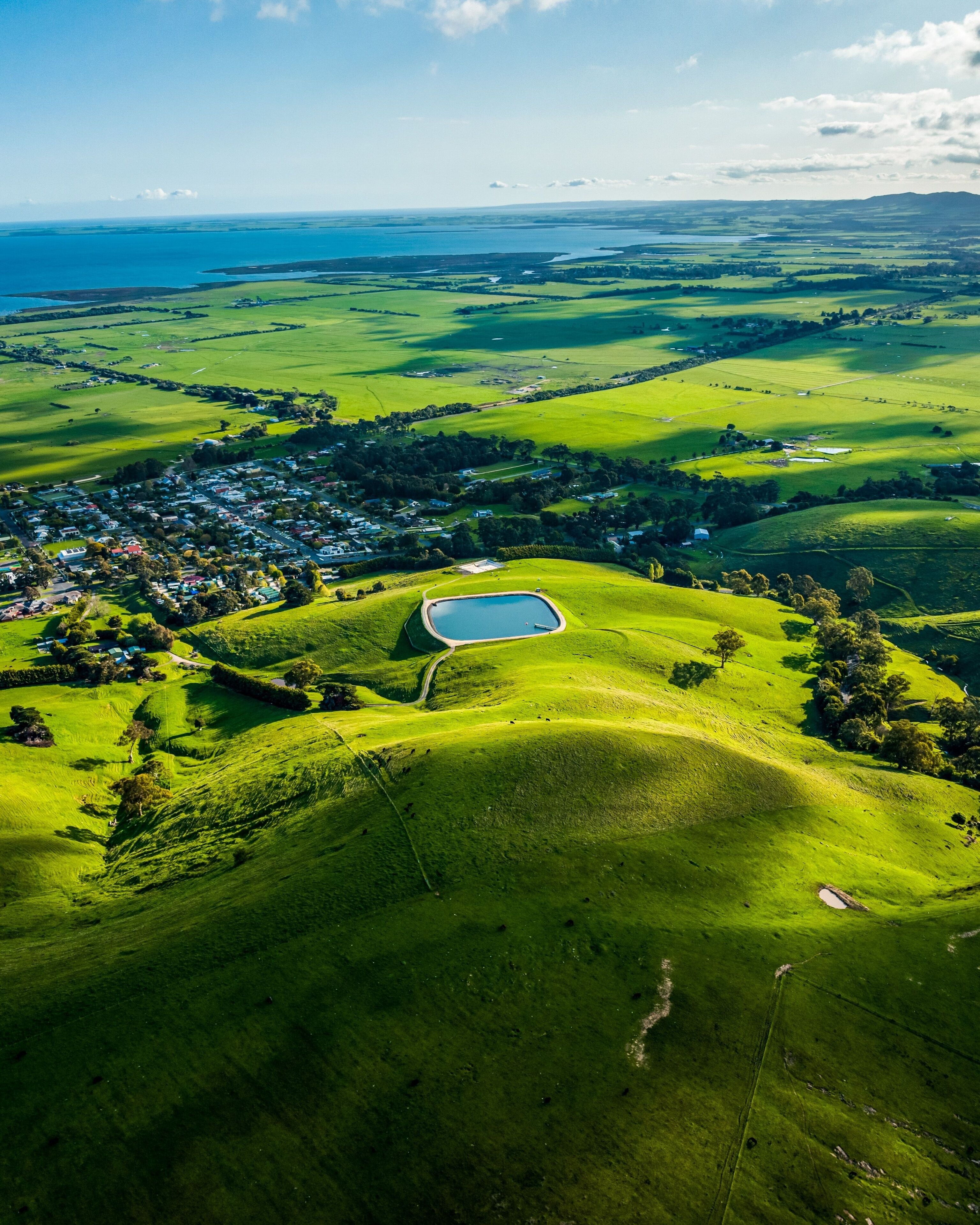 A lush green landscape with rolling hills, a small pond, and a distant village.
