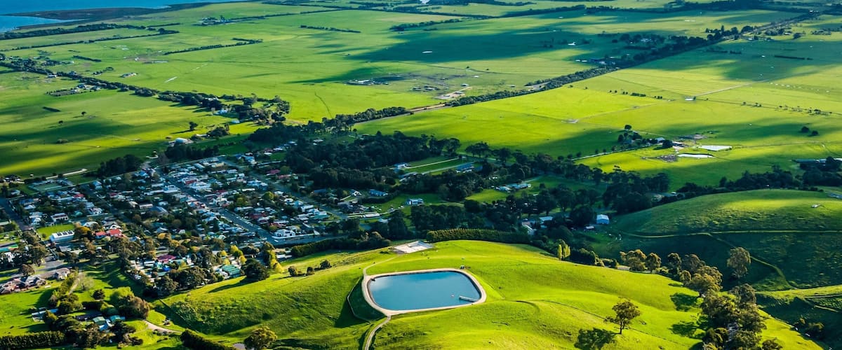 A lush green landscape with rolling hills, a small pond, and a distant village.