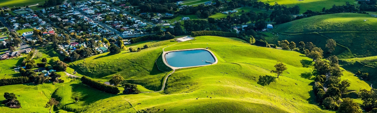 A lush green landscape with rolling hills, a small pond, and a distant village.