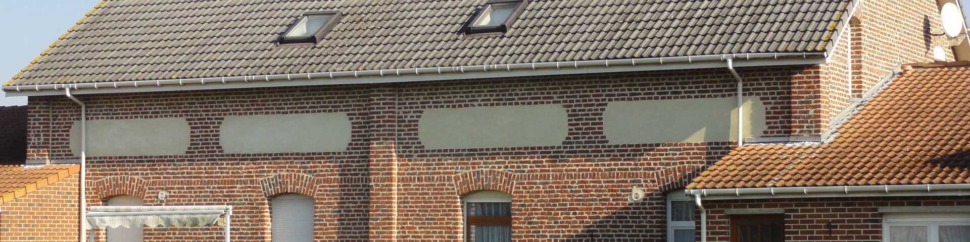 A brick house with a tiled roof and two satellite dishes.