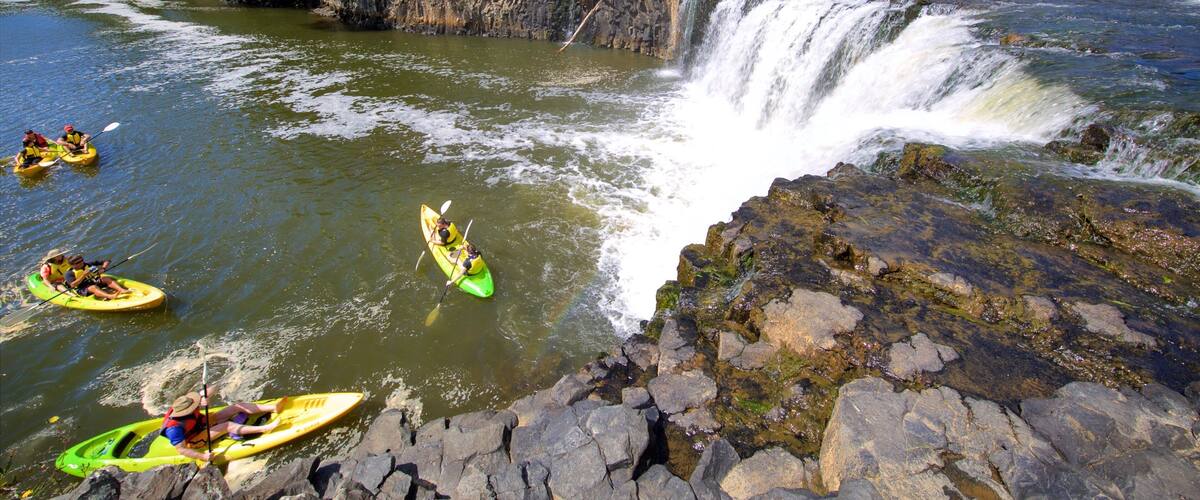 A river with a waterfall, kayakers, and a rocky riverbank.
