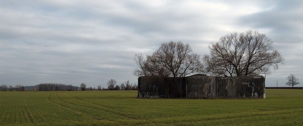 A rural landscape with a large, dilapidated barn in the center, surrounded by open fields and leafless trees.