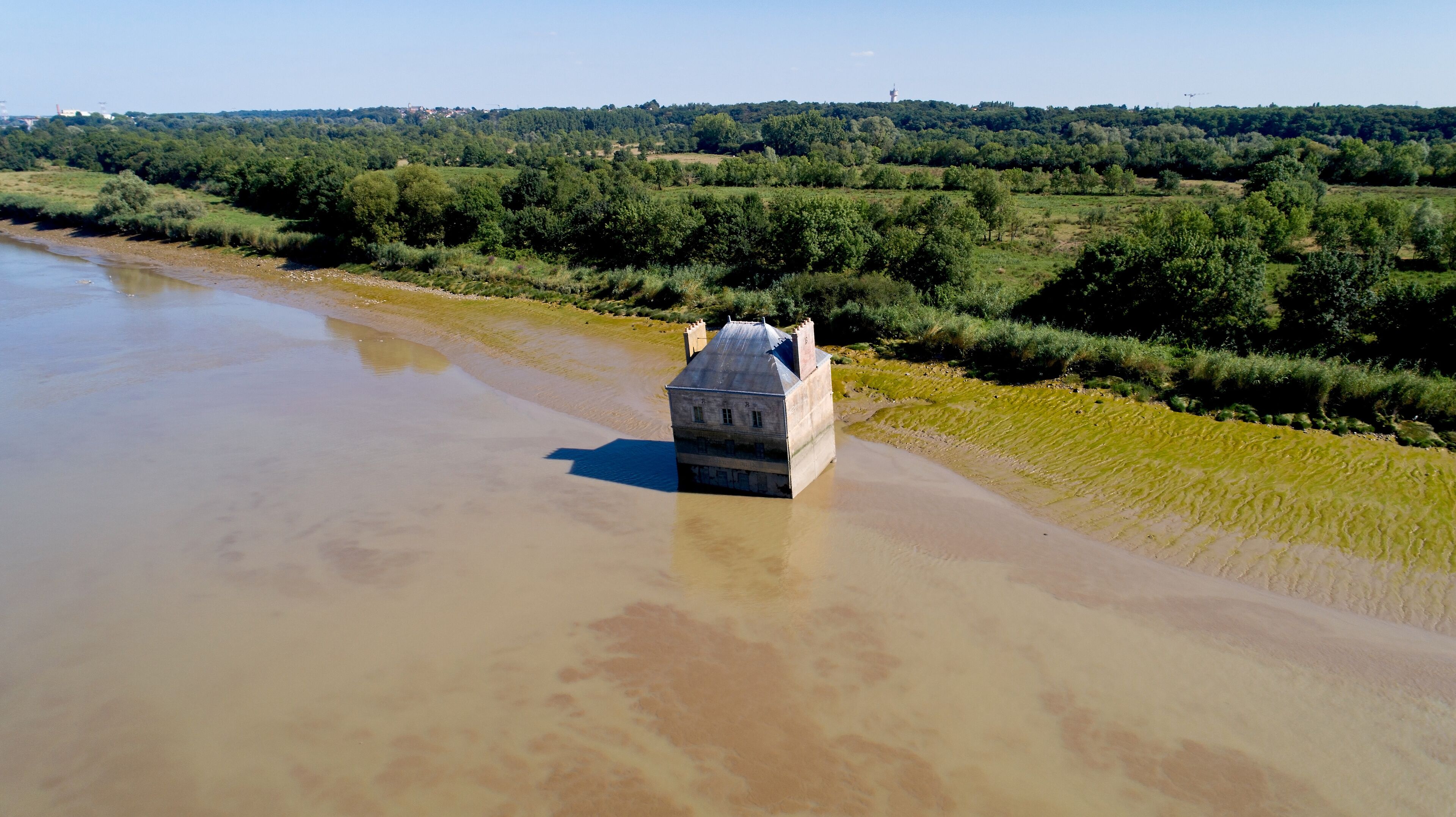A building partially submerged in a river surrounded by greenery.