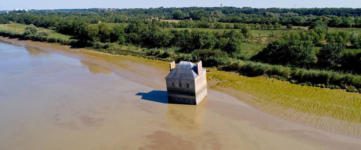 A building partially submerged in a river surrounded by greenery.