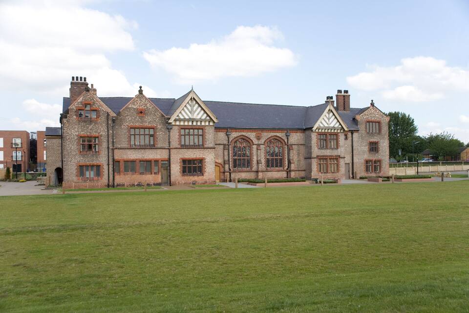 A large brick building with multiple windows and a grassy field in front.