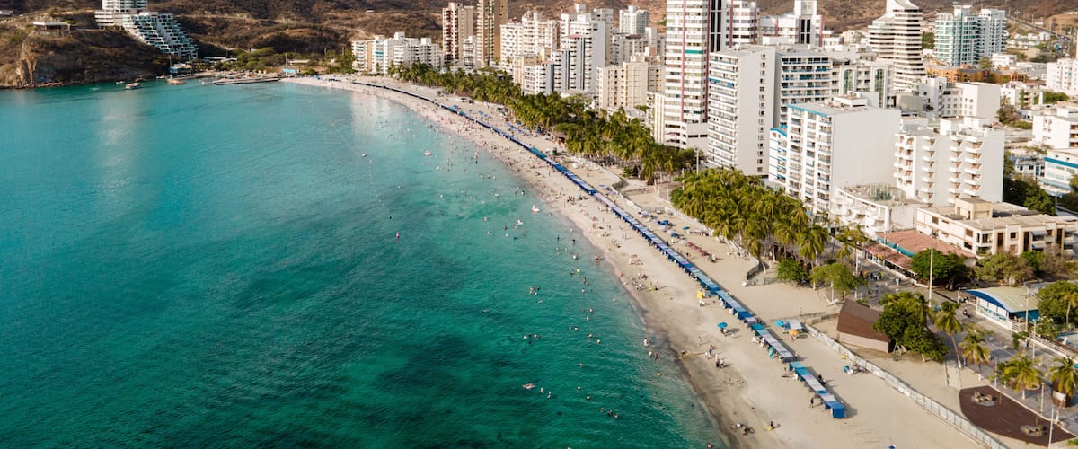 Une ville côtière dotée d’une plage, d’eaux turquoise cristallines et d’un paysage montagneux en arrière-plan.