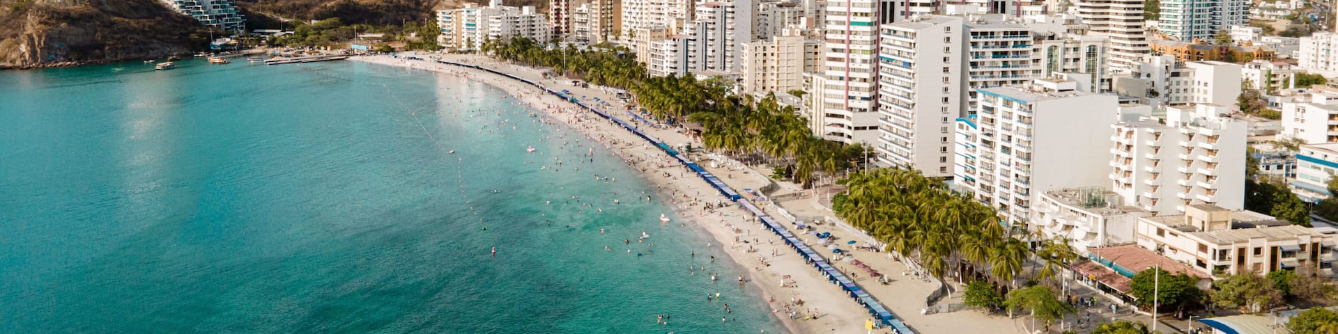 A coastal city with a beach, clear turquoise waters, and a mountainous backdrop.