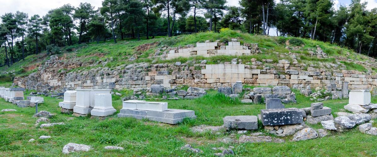 Ancient ruins with stone steps and scattered stone blocks on a grassy hillside.