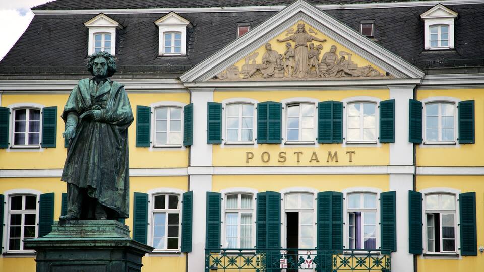 Eine Statue vor einem Gebäude mit grünen Fensterläden und dem Schriftzug 'POSTAMT' an der Fassade.