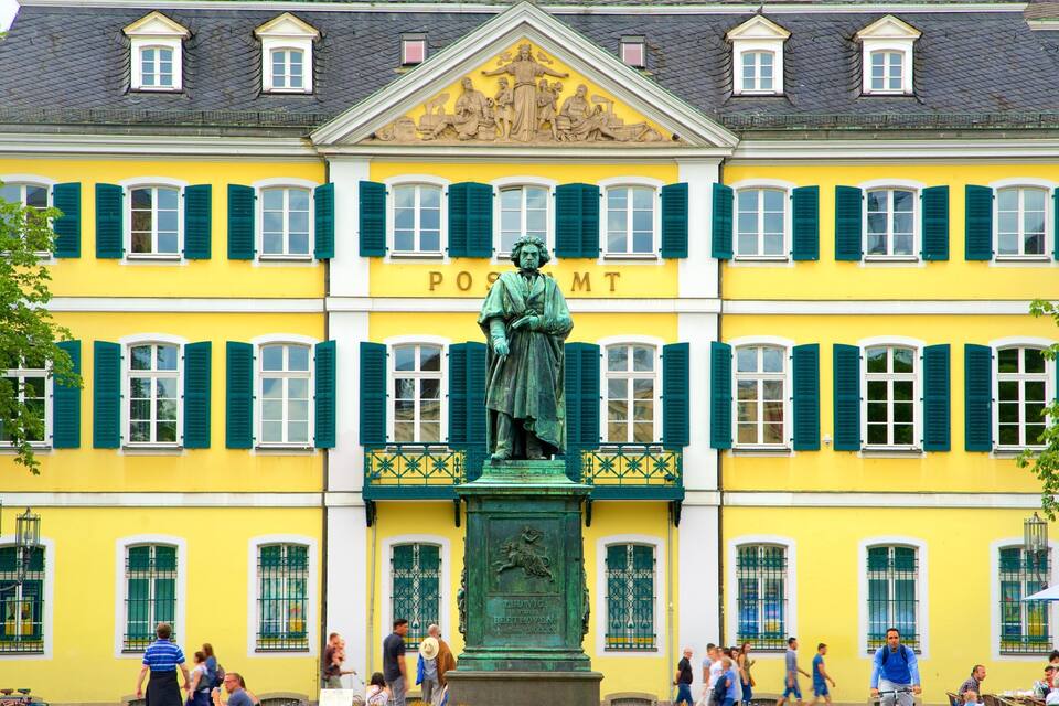 A yellow building with green shutters and a statue of a man in front.