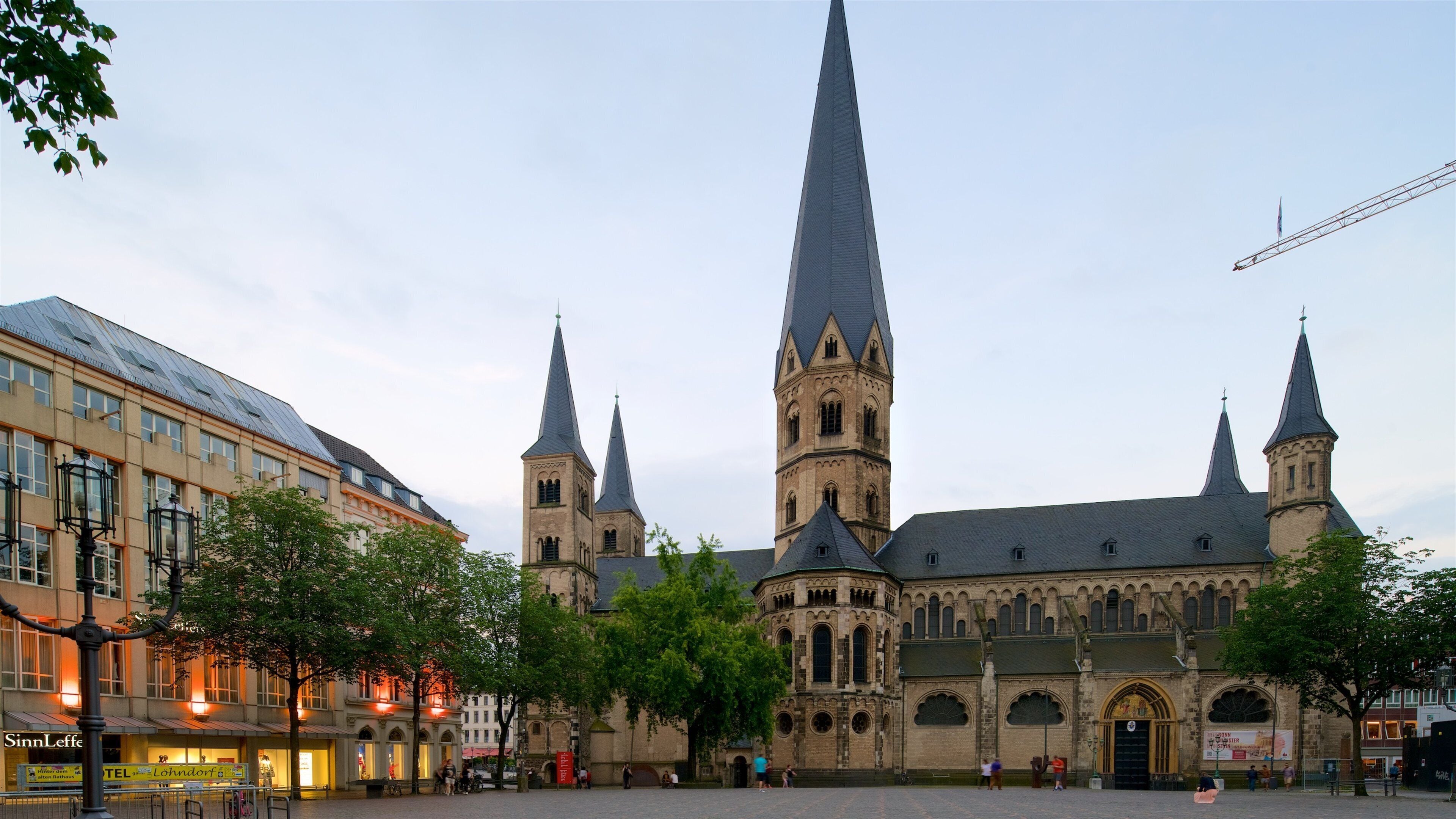 Una iglesia histórica con una alta torre central y dos torres más pequeñas, rodeada de edificios modernos y árboles.