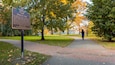 A park with a historical marker, trees with autumn leaves, and a paved path.