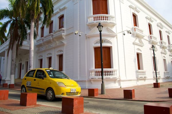 A yellow taxi parked in front of a white building with red pillars and a balcony.
