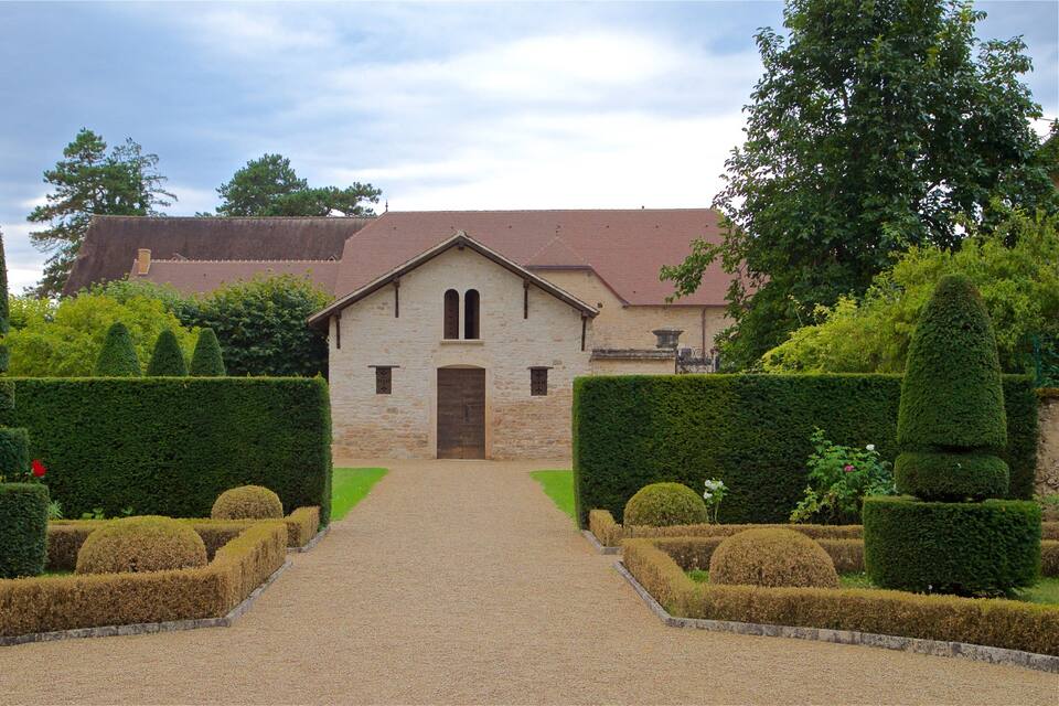 A stone building with a tiled roof, surrounded by well-manicured hedges and a gravel path leading to the entrance.
