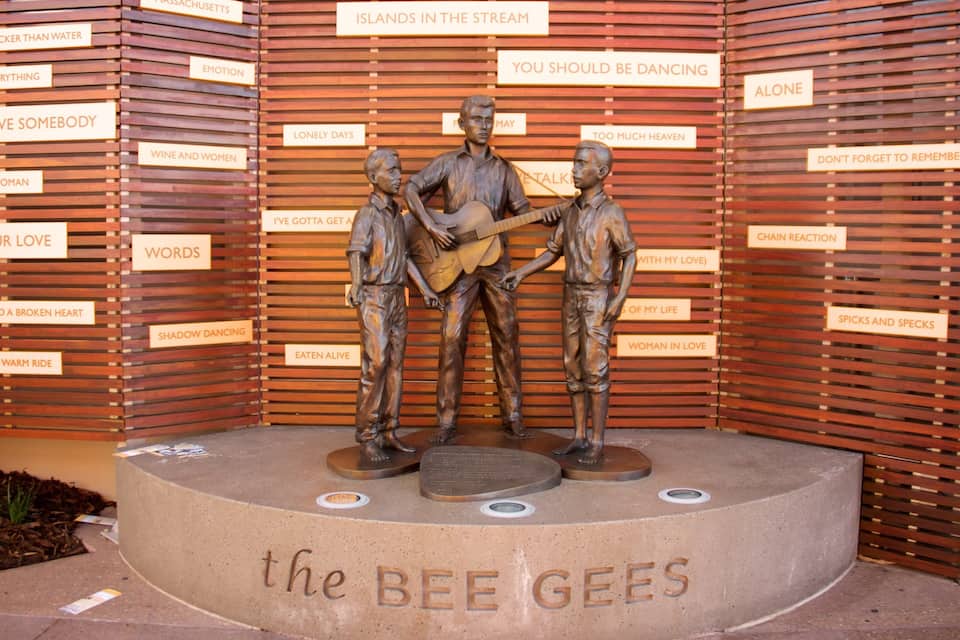 A bronze statue of The Bee Gees performing, surrounded by wooden slats with song lyrics.