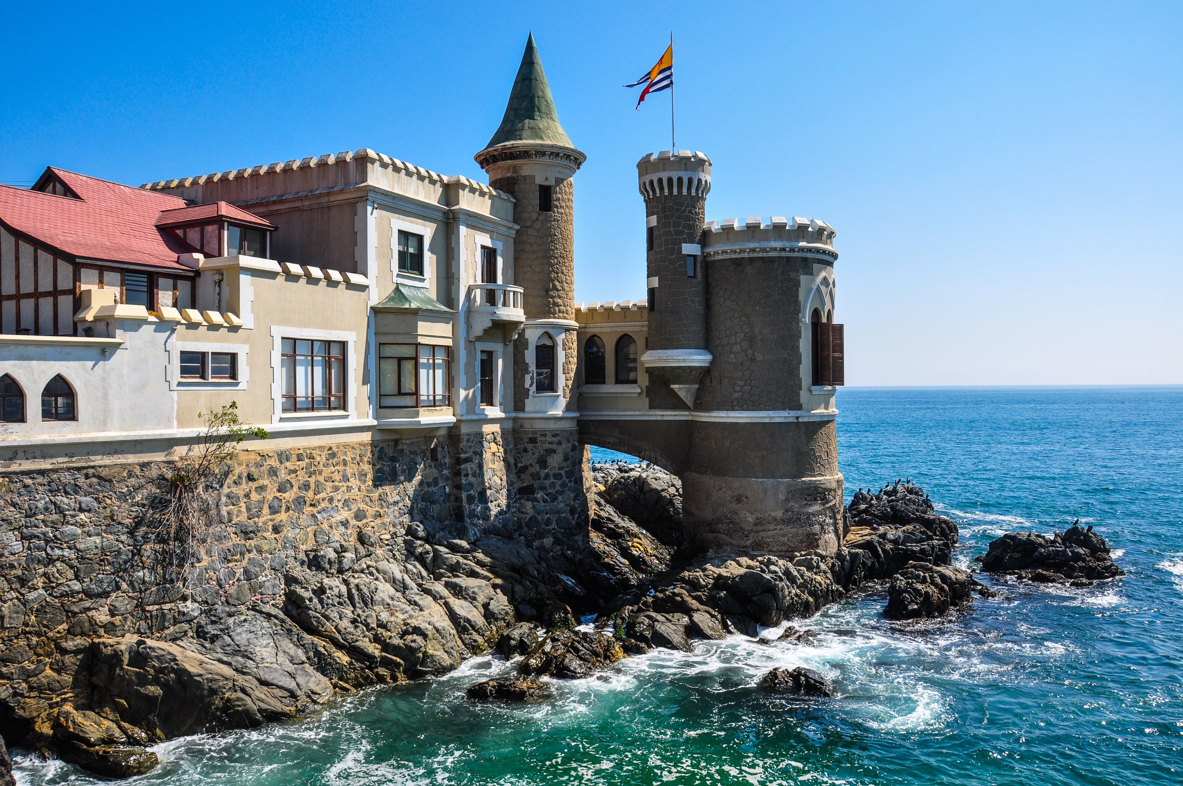 Un château situé sur la côte, avec un toit rouge, une tour en pierre et un drapeau.