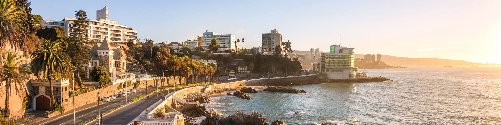 A coastal cityscape with a prominent road, buildings, and a rocky shoreline.