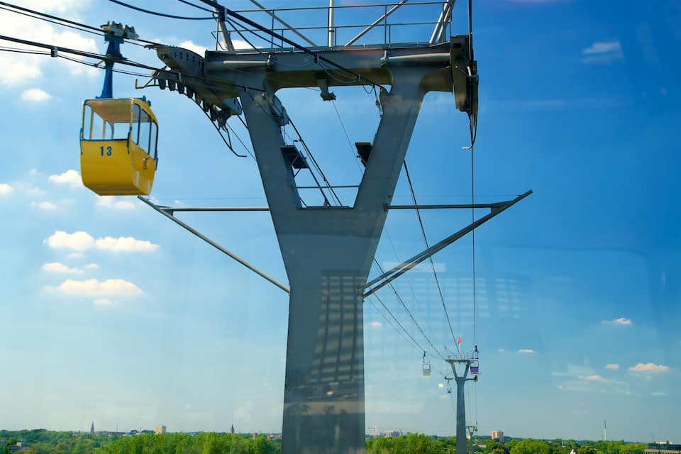 A yellow cable car suspended from a large metal structure against a clear blue sky.