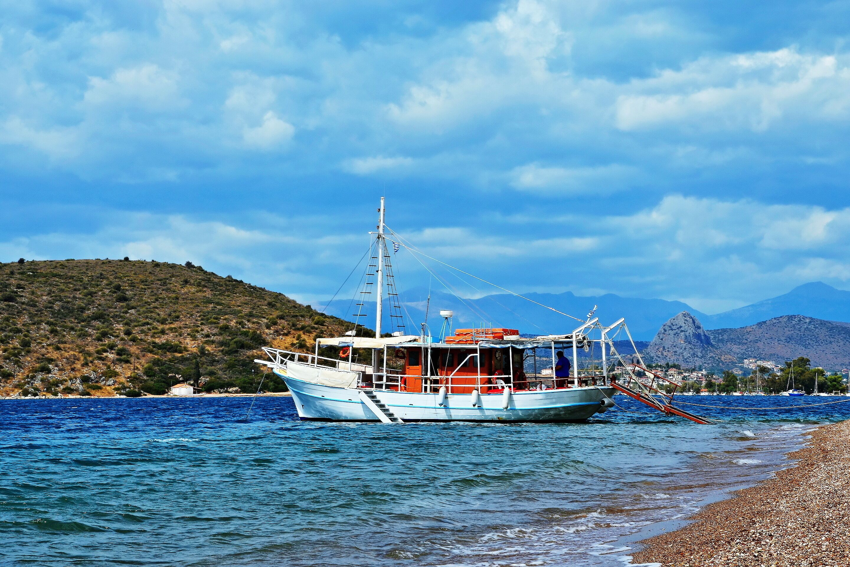 A fishing boat on calm waters near a rocky shore with mountains in the background.