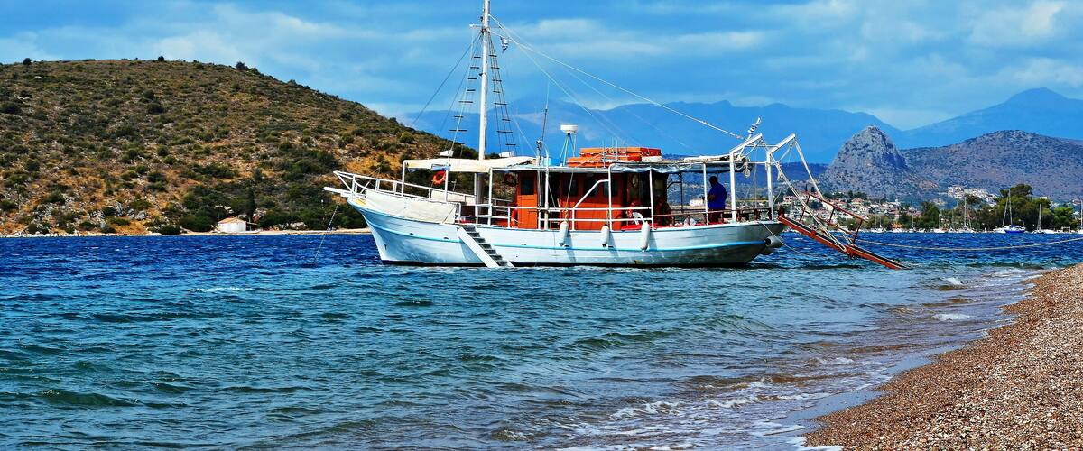 A fishing boat on calm waters near a rocky shore with mountains in the background.