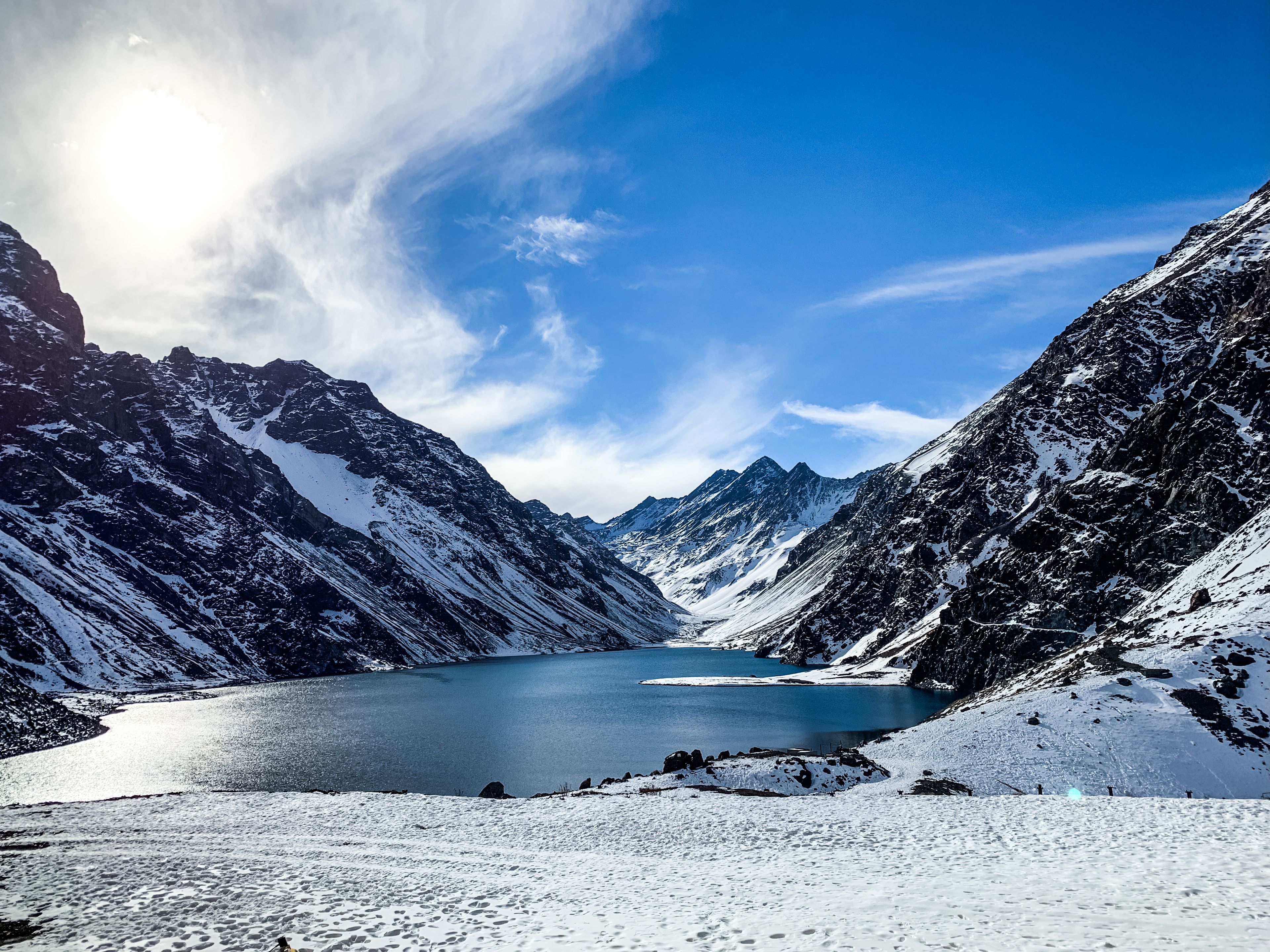 Paisagem montanhosa coberta de neve, com céu azul límpido e um lago.