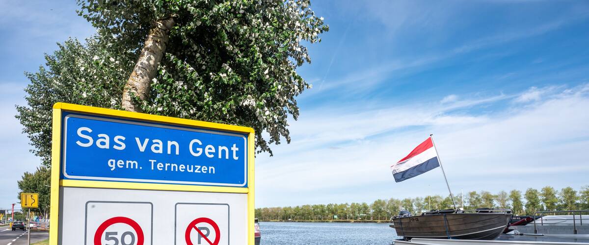 A sign with 'Sas van Gent' and 'gem. Terneuzen' text, a speed limit sign, a no parking sign, and a boat with a flag.
