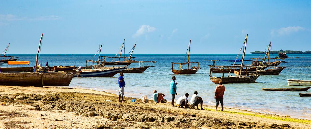 A beach with several boats anchored in the water and people on the shore.