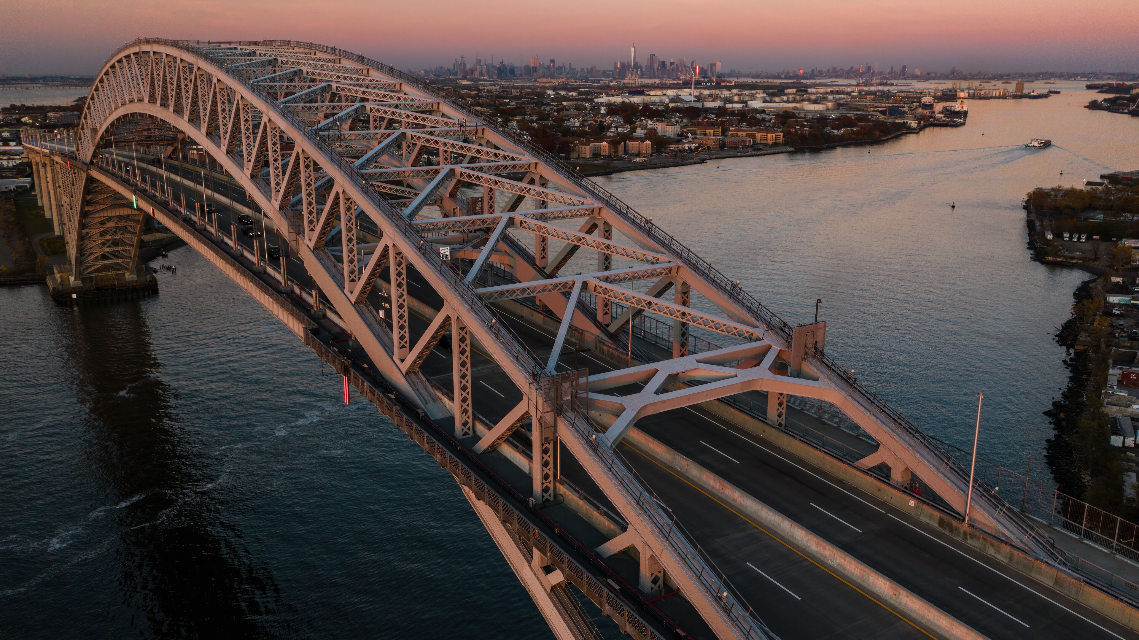 A large steel bridge spanning a wide river, with a city skyline in the background.