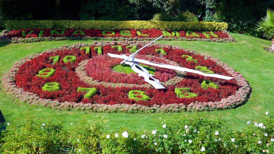 A large garden clock surrounded by colorful flower beds.