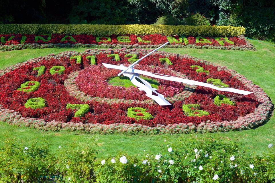 Un reloj de jardín grande rodeado de coloridas parterres.