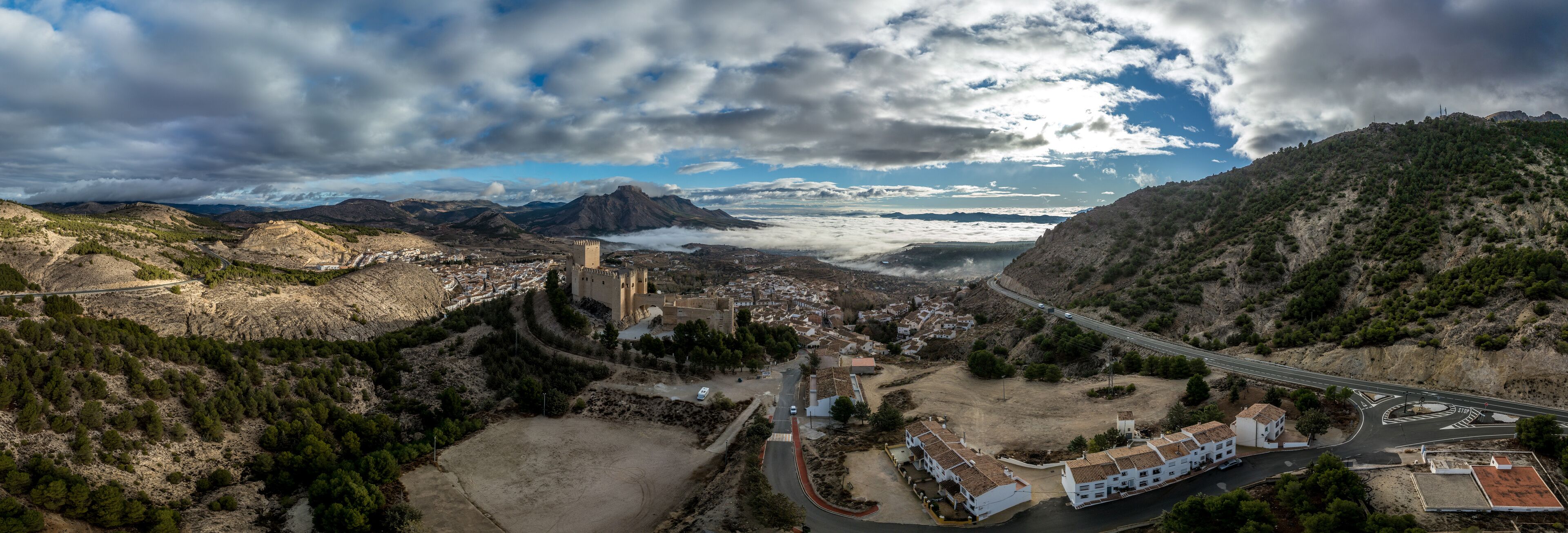 A mountainous landscape with a castle, a winding road, and a bridge.