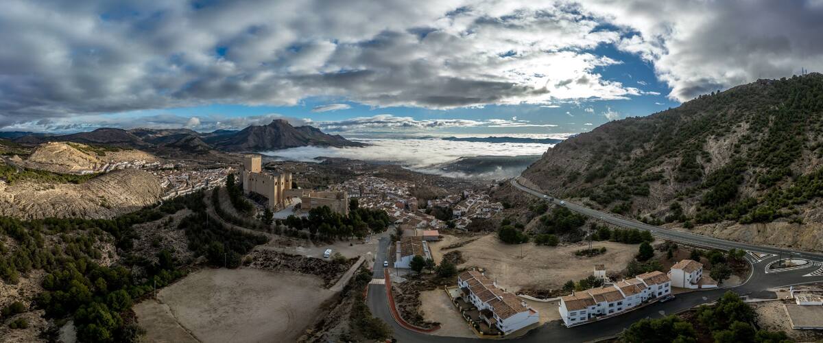 A mountainous landscape with a castle, a winding road, and a bridge.