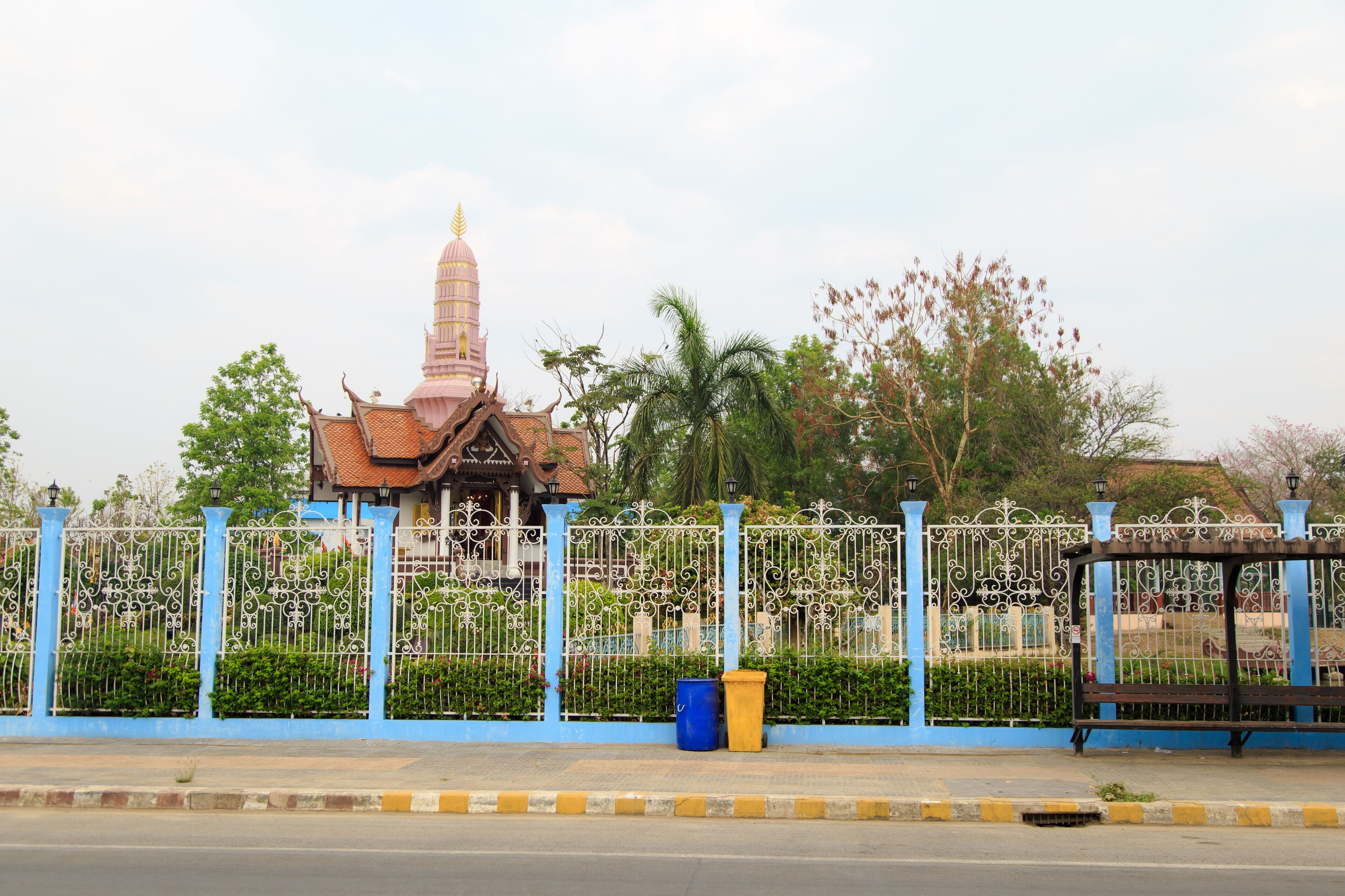 A temple with a tall spire, a blue fence, and a bench.