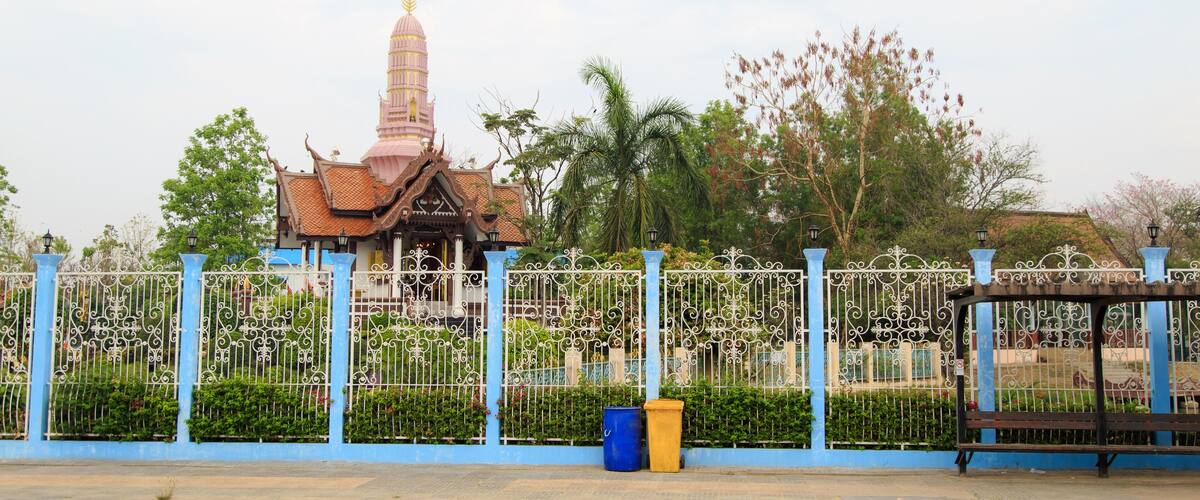 A temple with a tall spire, a blue fence, and a bench.