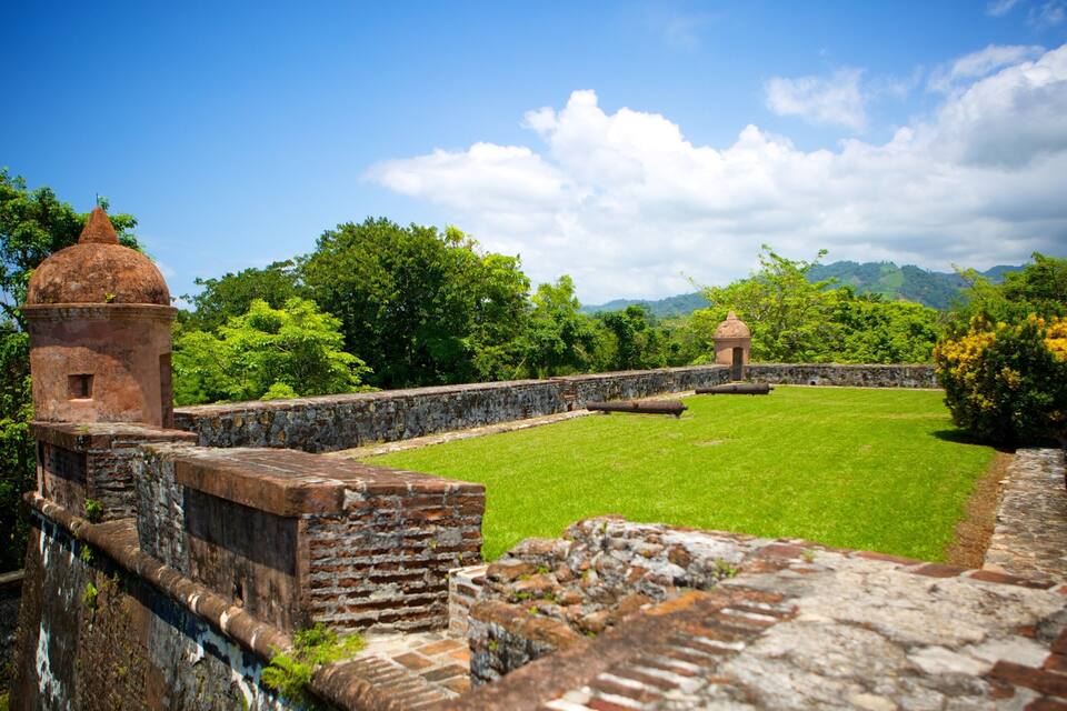 Una fortaleza histórica con un patio cubierto de césped, muros de piedra y una pequeña torre.