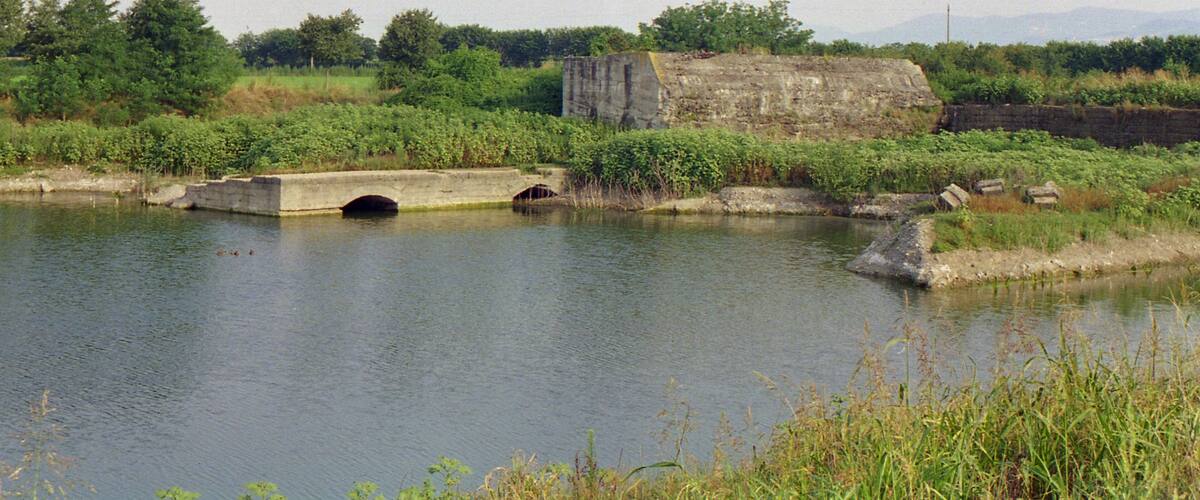 A river with a concrete bridge and a stone structure in the background.