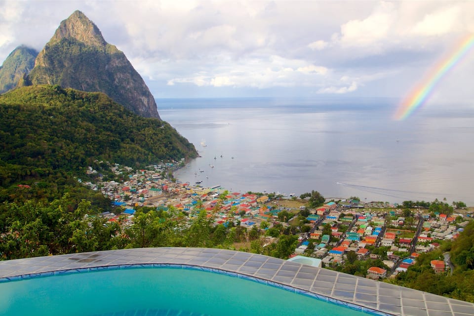 A coastal town with colorful houses, a mountain, and a rainbow over the sea.