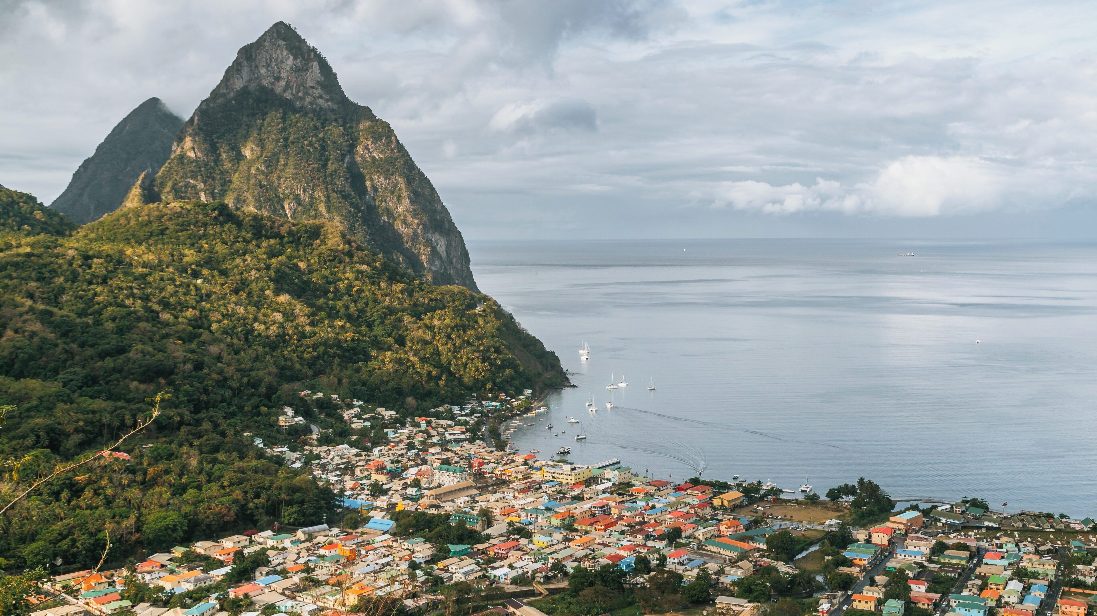 Gros Piton rises majestically above the vibrant town of Soufrière in St. Lucia, with calm waters and lush mountains in the background during a peaceful afternoon