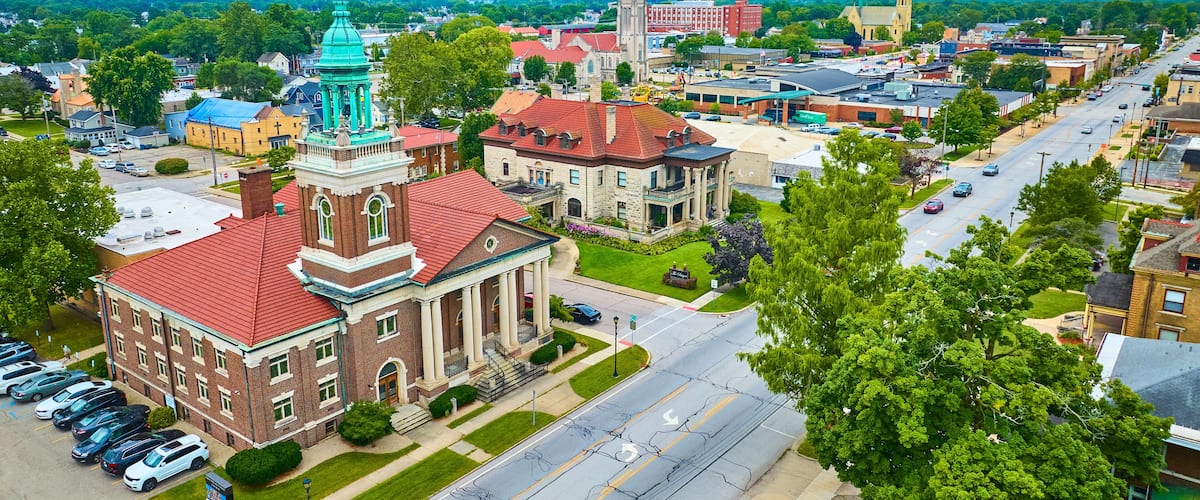 A town with a prominent red-roofed building with a green spire, surrounded by streets and other buildings.