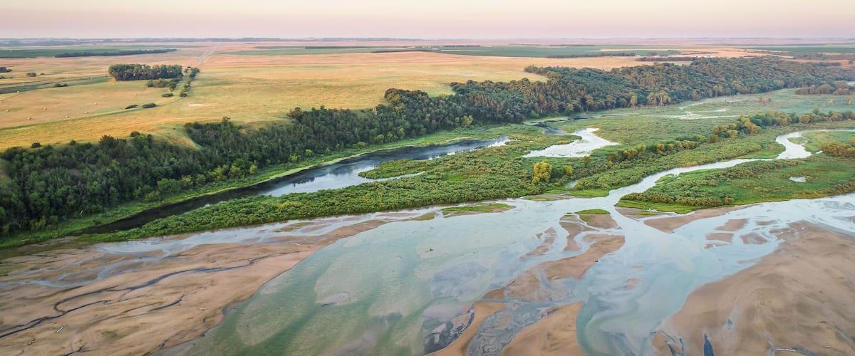 A river winding through a landscape with patches of water, green vegetation, and distant fields.