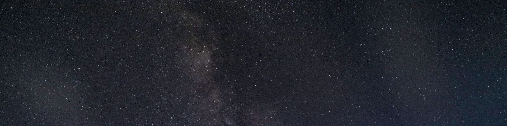 A night sky filled with stars and the Milky Way over a rocky landscape with unique formations.