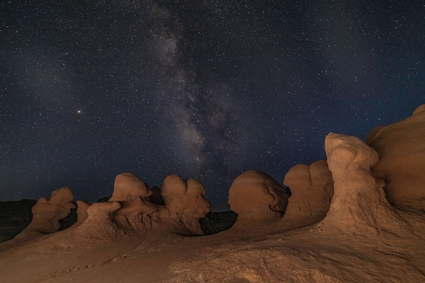 A night sky filled with stars and the Milky Way over a rocky landscape with unique formations.
