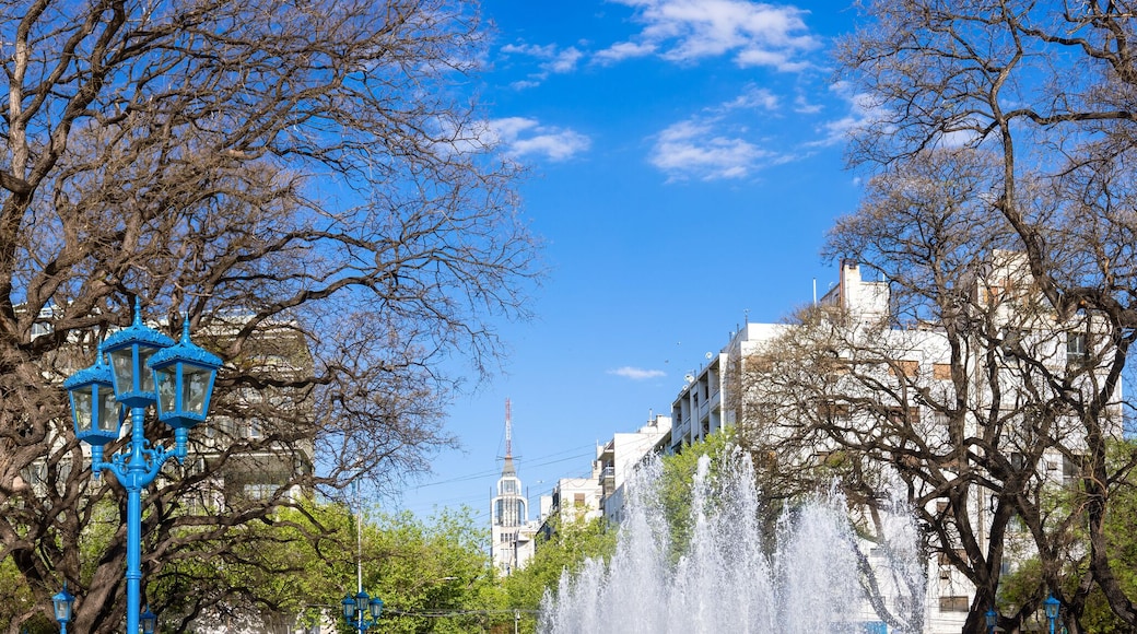 A park with a fountain, trees, and a building in the background.