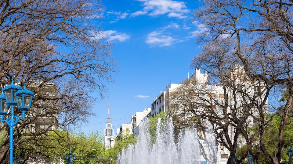 Un parque con una fuente, árboles y un edificio al fondo.
