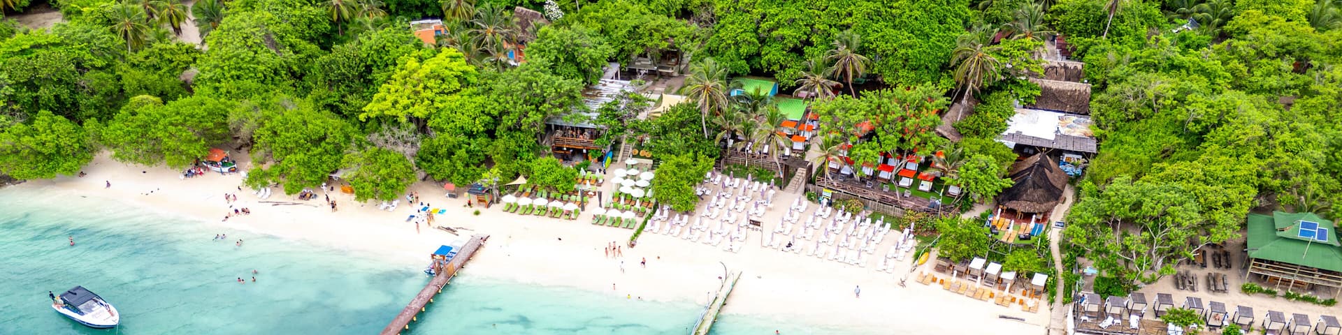 A tropical beach with clear turquoise waters, a pier, and a resort area with umbrellas and beach chairs.