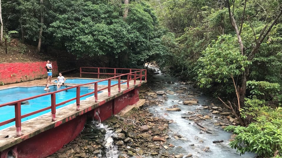 A bridge over a river with a pool on one side and a rocky stream on the other.