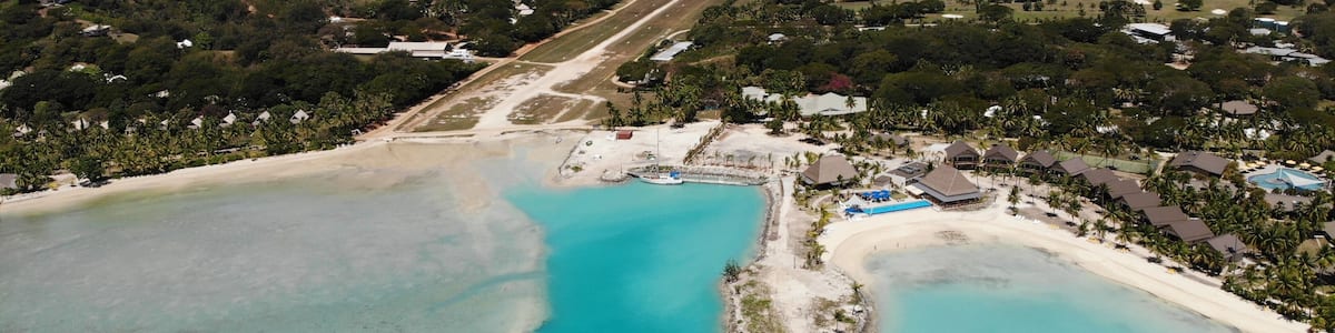 An aerial view of a coastal area with clear turquoise waters, a sandy beach, and a mix of residential buildings and greenery.