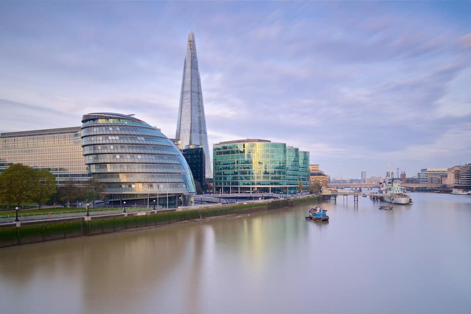 A river with modern buildings, including a distinctive tall skyscraper, and a bridge in the background.