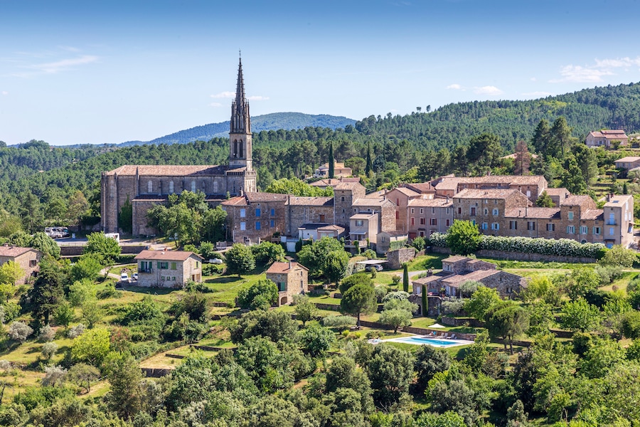 Une ville historique abritant une église remarquable, reconnaissable à son clocher imposant, et entourée d’une végétation luxuriante, avec en toile de fond un paysage montagneux.